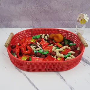 Red imitation rattan storage basket with wooden handles detail view, filled with snacks.