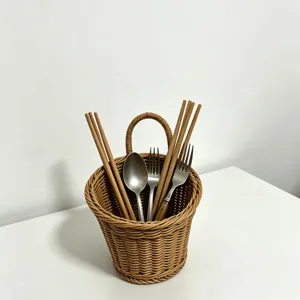 Close-up detail of a woven hanging storage basket holding kitchen utensils on white table.