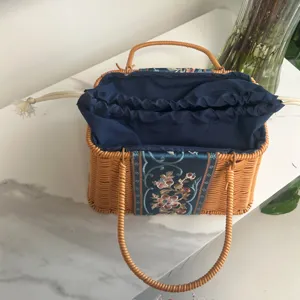 Trapezoid woven handbag with embroidered blue panel and drawstring lining for stylish daily use.