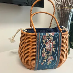 Woven rattan handbag with blue embroidered fabric panel, double handles and drawstring.