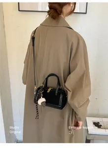 Vista detallada de un elegante bolso cruzado negro tipo almohada con dije de peluche.
