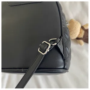 Gros plan d'un sac à dos matelassé noir montrant la boucle métallique réglable et la sangle.