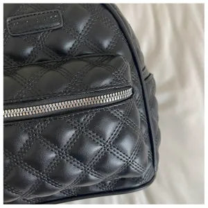Détail du sac à dos en cuir matelassé noir avec poche zippée et logo gravé.