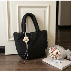Schwarze gesteppte Tasche Detail mit süßem Blumenanhänger im sauberen Zimmer, Alltag Stil.