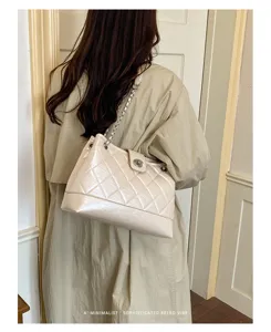 Detailansicht der beigen gesteppten Schultertasche mit Metallkette und Drehverschluss.