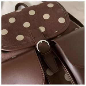 Brown polka dot backpack detail view, featuring suede flap, leather pockets and sleek metal buckle.