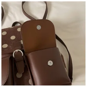 Brown polka dot backpack front pocket detail, leather flap and metallic snap button design.