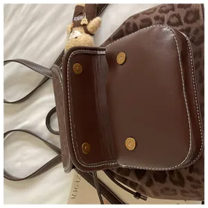 Brown leopard print women casual backpack detail view featuring leather flap and bear pendant