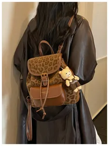 Detail shot of stylish leopard print backpack with cute bear pendant and brown leather trim.