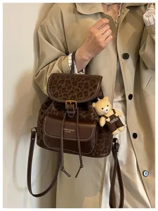 Detailed view of trendy leopard print leather backpack with cute bear pendant and front pocket.