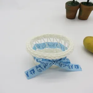 Mini white woven plastic flower basket detail view featuring light blue baby boy ribbon bow.