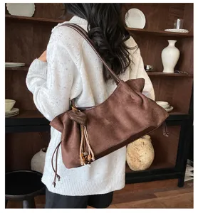 Detailed view of a retro brown suede shoulder bag with tassel charm and cozy aesthetic backdrop.