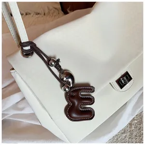 Dettaglio borsa a tracolla intrecciata bianca con ciondolo in pelle e perline di metallo.