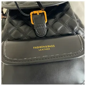 Detailed view of black quilted leather backpack, gold metal buckle and front pocket details.