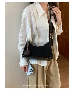 Detailed shot of black suede shoulder underarm bag with leather base and woven charm.