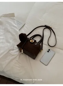 Élégant sac bandoulière en suédine marron foncé avec fermoir métallique et pompon duveteux.