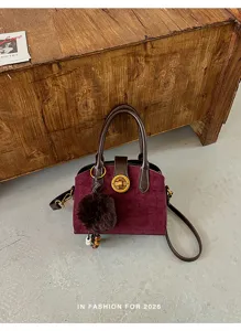 Vue rapprochée du sac à main en daim bordeaux avec bordure marron et fermoir tournant.