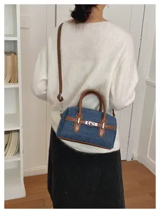 Denim top handle shoulder bag with brown leather trim and metal turn-lock closure for daily wear.