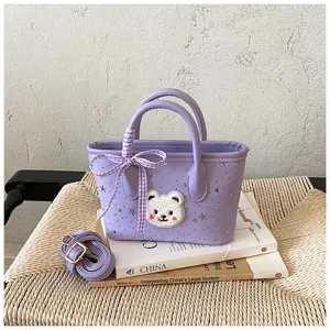 Close-up view of a purple women handbag featuring a cute bear patch and chic plaid ribbon.
