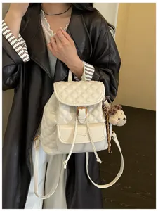 White quilted leather backpack detail view with front pocket and cute plush charm.