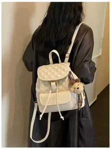 Detail view of a chic white quilted leather backpack with a cute bear pendant and drawstring.