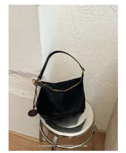 Close-up detail of a minimalist black suede hobo shoulder bag with chic zipper and tassel charm.