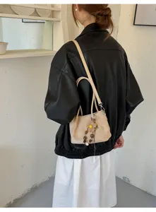 Detail shot of a casual beige shoulder bag with cute floral bead pendant, worn by model.