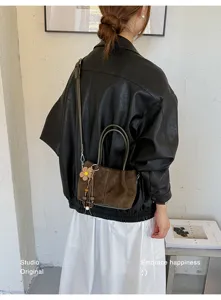 Stylish brown suede crossbody bag for women, featuring a chic floral charm and top handles.