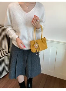 Close-up view of the yellow suede shoulder bag with cute flower pendant detail in scene.