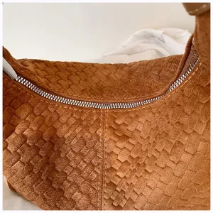 Detalle de bolso de ante tejido marrón, con patrón de textura y cremallera metálica.