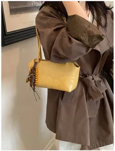 Vista detallada del bolso de hombro amarillo minimalista con colgante de cuentas de madera.