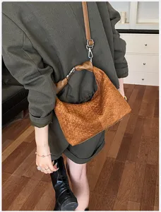 Vista de primer plano detallada de un bolso hobo de cuero tejido marrón con herrajes metálicos.