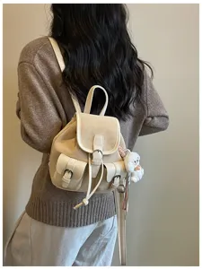 Detalles de una mini mochila en color beige con bolsillos delanteros y colgante de peluche.