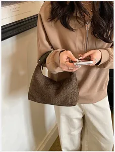 Vista detallada de un elegante bolso de hombro tejido marrón sostenido por un modelo chic.