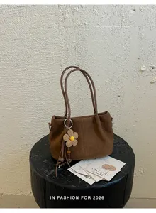 Brown suede shoulder bag detail showing texture and flower charm pendant on stool.