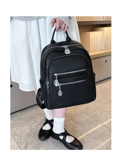 Close-up detail of the black leather backpack showing multiple zipper pockets and metal pendants.