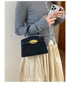 Detail shot of a minimalist retro black handbag with gold turn-lock and top handle.