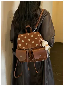 Detail view of brown polka dot suede backpack with dual front pockets and dog charm.