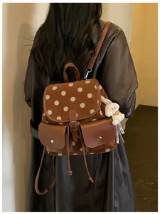 Close-up view of the brown polka dot backpack with front pockets and cute puppy pendant charm.