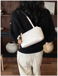 Detalle de bolso de hombro blanco con diseño minimalista y colgante de flor de madera.