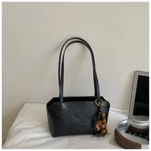 Vista en detalle del bolso de hombro minimalista de cuero negro con abalorio de madera.