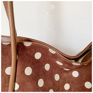 Détail de sac cabas à pois en daim marron, avec texture douce et poignées en cuir.