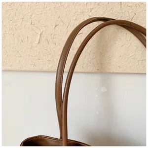 Gros plan détaillé des bretelles de sac cabas en cuir marron et design d'ouverture minimaliste.