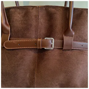 Close-up detail of stylish brown suede tote bag with leather belt and silver metal buckle.