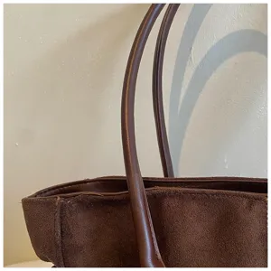 Close-up detail of brown suede tote bag showing leather handles and premium material texture.