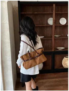 Brown suede tote bag detail, retro shoulder bag with dark straps and buckle decoration.