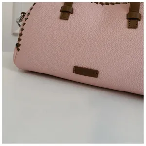 Detailopname van roze lederenhandtas met bruine stiksels en logo patch voor dames.