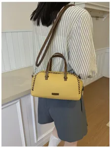 Gedetailleerd overzicht van de gele Boston handtas met bruine stiksels en dubbele handvatten.