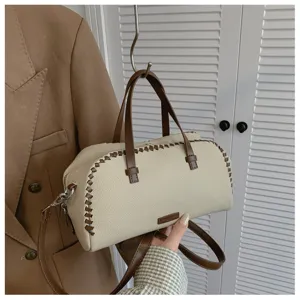 Detailopname van beige boston tas met bruine stiksels, handvatten en schouderband.