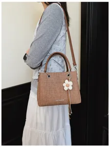 Vista detallada de elegante bolso de hombro texturizado marrón con bonito colgante de flor.